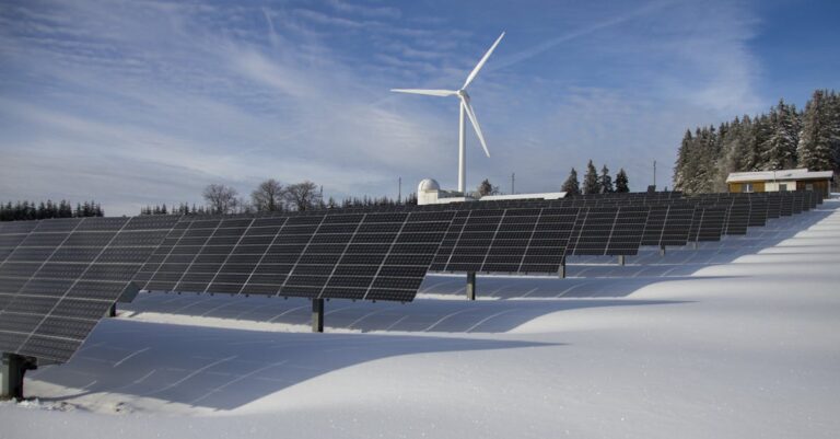Solar panels and wind turbine in a snowy landscape, showcasing renewable energy sources.